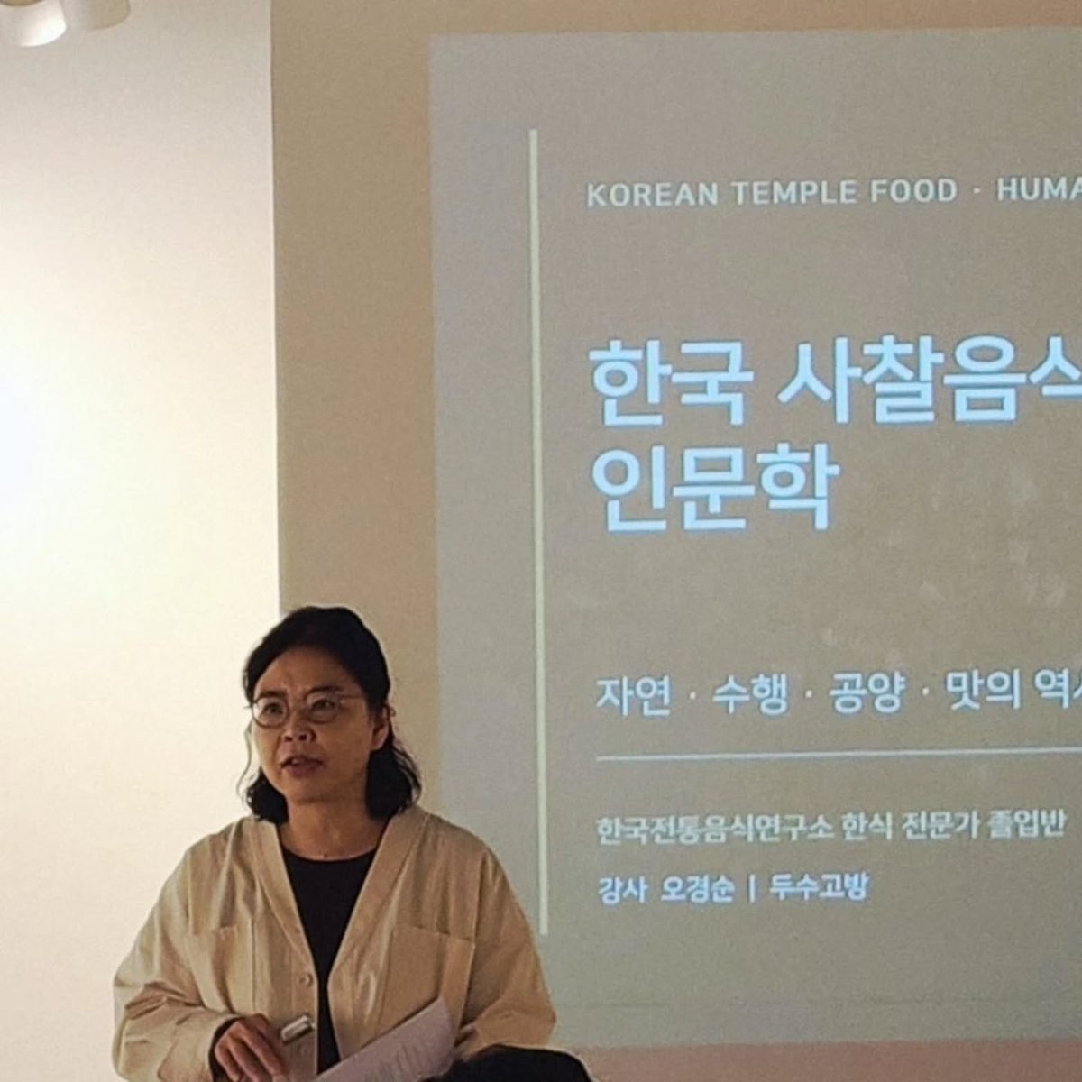 「한국 사찰음식 인문학」 화면 앞에서 강의하는 오경순. 화면에 강사 오경순, 두수고방이라고 적혀 있다